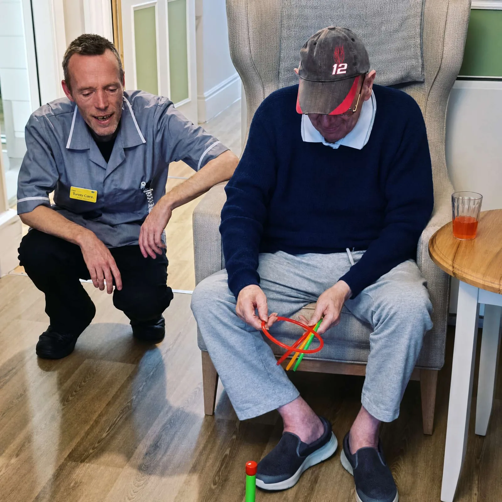 A carer sharing a warm, unhurried conversation with a resident in the lounge at Belmont Castle