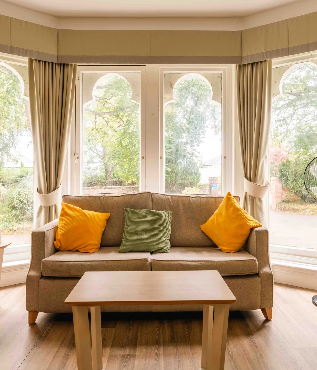 A quiet sitting room, a sofa and armchairs in a bay of arched windows