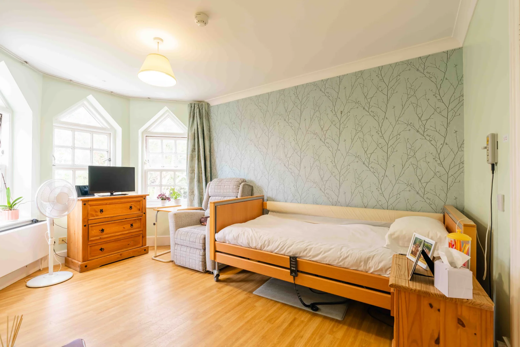 A bedroom under pointed Gothic windows, with a profiling bed and a patterned feature wall